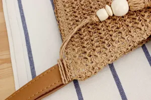 Close-up detail view of a stylish straw woven casual women bag with leather strap and beads.