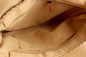 Interior detail of beige woven women's handbag with zipper pocket and lining structure.
