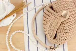 Handmade crochet shoulder bag detail showing fine texture, woven strap and elegant pearl chain.