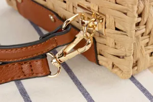Detailed view of straw woven crossbody bag hardware, golden metal clasp and PU leather strap.