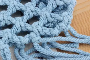 Close-up detail of light blue woven macrame bag showing intricate mesh and fringe texture.