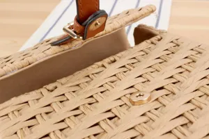 Handmade woven straw handbag detail showing exquisite texture and brown leather strap.