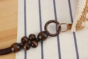 Close-up detail of woven shoulder bag strap with wooden beads and gold hardware craftsmanship.