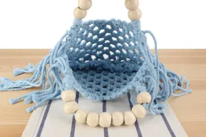 Detail shot of blue macrame woven hollow bag with natural wooden bead handles and fringe.