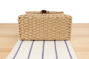Closeup detail of handmade woven straw box bag featuring metal clasp on wooden table surface.