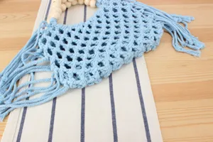 Light blue woven hollow shoulder bag with wooden bead handle and tassel boho chic design.