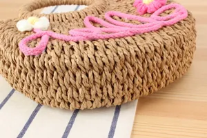Handmade woven straw round handbag detail view with cute flower and pink yarn script design.