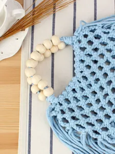 Chic light blue handmade macrame woven handbag with wooden bead handles for casual seaside vacation.