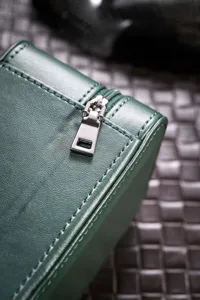 Close-up detail of green leather watch storage box with fine stitching and silver zipper.