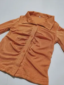 Detailed close-up shot of the orange ribbed ruched long sleeve collared shirt with buttons.