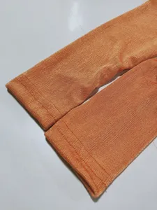 Close-up detail of women's orange pleated cardigan sleeve, showing fine fabric and neat stitching.