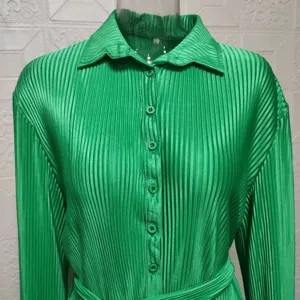 Detail shot of green pleated long sleeve shirt dress with matching buttons and belt.