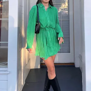 Green pleated long sleeve shirt dress detail view, elegant casual midi dress with matching waist belt.