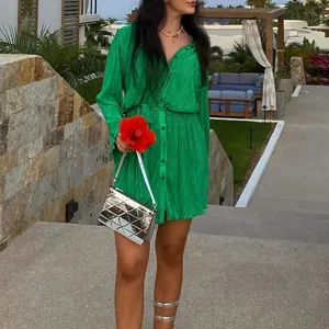 Green pleated shirt dress detail featuring long sleeves, front button closure and fabric belt.
