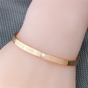 Detailaufnahme eines roségoldenen Edelstahl-Armreifs mit funkelndem Kristall und Liebestext.