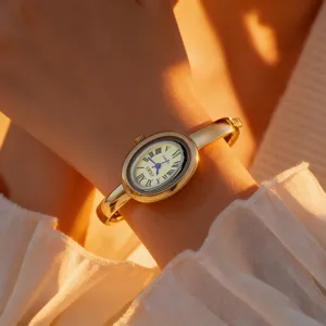 Dettaglio ravvicinato di un orologio bracciale ovale dorato da donna con numeri romani al polso.