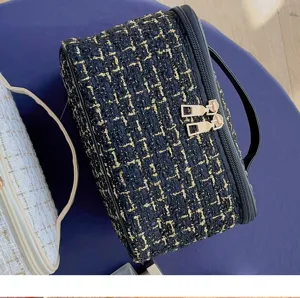 Close-up of black tweed cosmetic bag with gold hardware, textured fabric and dual zippers.