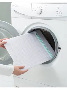 Detailed view of white mesh laundry bag with green zipper being placed into washing machine.