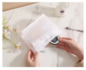 Vista detallada de la bolsa cosmética de malla blanca abierta en mesa de mármol con maquillaje.