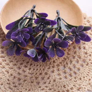 Detailed closeup of artificial purple flower stems in wooden bowl on crochet lace mat.