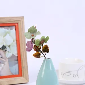 Artificial flower branch with colorful simulation leaves in small ceramic vase for home decor.