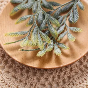 Detailed close-up of artificial green plant leaves branch on wooden plate and mat.