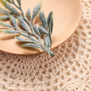 Closeup shot of artificial green plant leaf accessory displayed on wooden plate and lace mat.