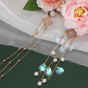 Close-up detail of decorative hair accessory with gold chains, shell sequins and white beads.
