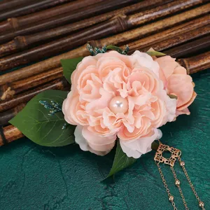 Close-up of pink artificial flower hair clip with pearl center, green leaves and gold chains.