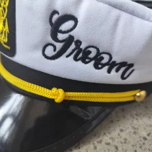 Close up detail of white groom captain hat with black embroidery and yellow cord trim.