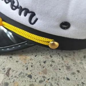 Detail view of white cotton sailor hat with gold button and black embroidery for parties.