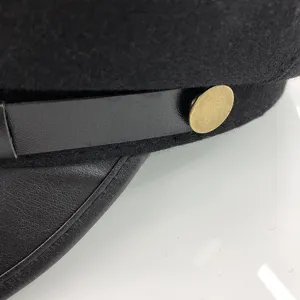 Close-up detail of black flat top military cap featuring chic leather strap and brass button.