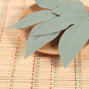 Detail shot of artificial green leaves in a wooden plate on bamboo mat for home decor.