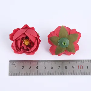 Detail shot of red artificial rose flower heads with a metal ruler showing size proportions clearly.