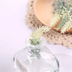 Botella de vidrio transparente con rama de planta artificial, accesorio para fotos.