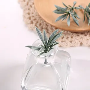 Hojas de plantas verdes artificiales en una botella de vidrio transparente decorativa.