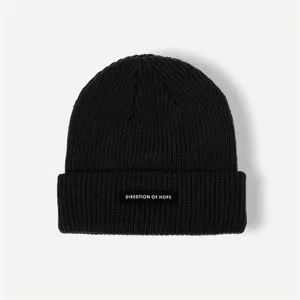 Detailed shot of a black winter knit beanie hat, featuring a woven label with text accent.