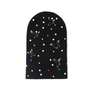 Close-up detail of black knit beanie decorated with sparkling rhinestones, pearls and punk safety pins.
