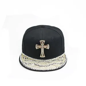 Casquette hip-hop noire avec croix en strass et visière texturée dorée étincelante.