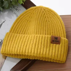 Close-up of yellow knitted beanie with brown leather tag, winter warm thermal cap details.