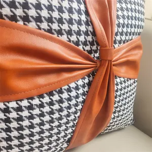 Close-up of black white houndstooth velvet cushion detail with brown leather bow accent.