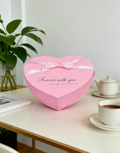 Detailaufnahme einer rosafarbenen herzförmigen Geschenkschachtel mit weißer Schleife für Anlässe.