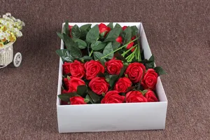 Close-up detail of artificial red soap roses with green leaves arranged neatly in a white box.