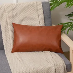 Detail view of brown faux leather lumbar pillow on cozy grey armchair with knitted blanket.