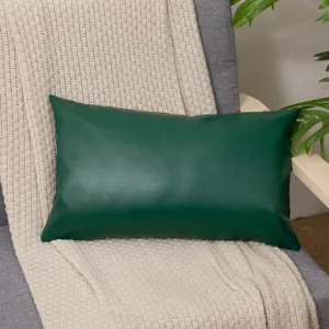 Dark green leather cushion detail in cozy home setting with beige knit blanket and plant.