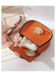 Vista dettagliata del ciondolo per mini borsa a sella arancione con AirPods e stella.