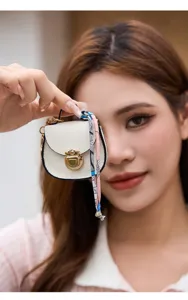 Dettaglio in primo piano di una mini borsa a sella bianca con charm e chiusura metallica.