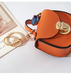 Mini borsa a sella in pelle arancione portachiavi con dettagli dorati e nastro colorato.