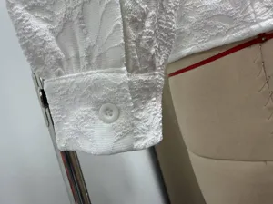 Detailed view of white textured long sleeve top cuff with button closure, elegant style.