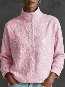 Close-up detail of a pink long-sleeve top featuring intricate white floral embroidery and buttons.